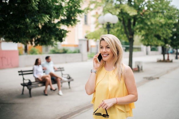 Porträt der lächelnden stilvollen Frau, die draußen am Telefon spricht.