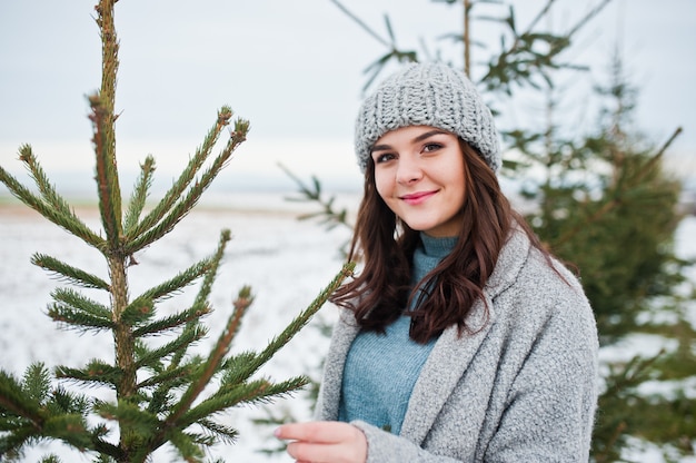 Porträt der leichten Frau im grauen Mantel und im Hut gegen den Weihnachtsbaum im Freien.