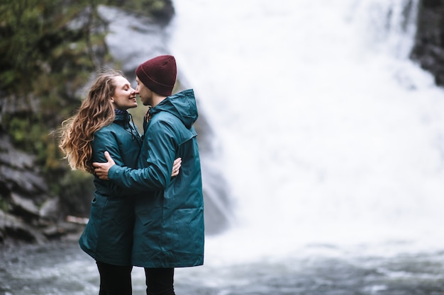 Porträt der Liebenden in den grünen Regenmänteln, die auf einem Wasserfall stehen