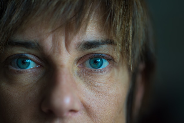 Porträt der mittleren Greisin mit blauen Augen, nahem hohem und selektivem Fokus auf einem Auge, sehr flache Schärfentiefe. Dunkle Einstellung, getöntes Bild.