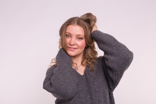 Porträt der modischen jungen blonden Frau mit dem lockigen Haar in der grauen Strickjacke