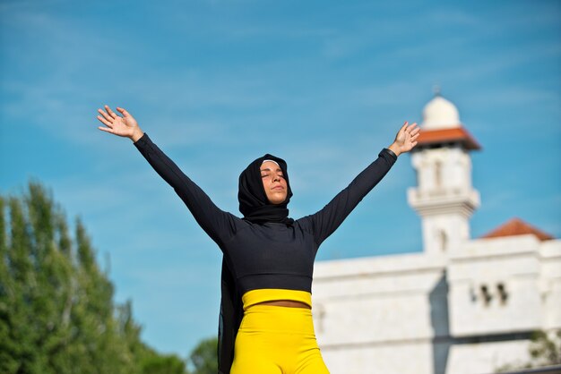 Porträt der muslimischen Frau, die einen Hijab trägt, der mit Moscheehintergrund lokalisiert wird. Horizontale Ansicht der freien arabischen Frau im Freien. Muslimische Frauen und Gleichstellungskonzept.