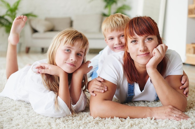 Porträt der Mutter mit ihrer Tochter und ihrem Sohn, die auf dem Teppich auf dem Boden des Hauses liegen