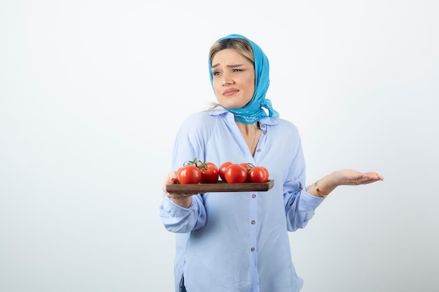 Porträt der netten Frau im blauen Schal, der Holzbrett der roten Tomaten hält