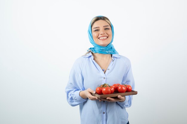 Porträt der netten Frau im blauen Schal, der Holzbrett der roten Tomaten hält