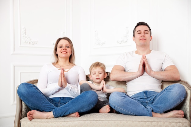 Porträt der niedlichen Familie mit dem kleinen Sohn, der in der Lotushaltung auf Sofa meditiert