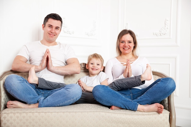 Porträt der niedlichen Familie mit dem kleinen Sohn, der in der Yoga-Pose auf Sofa aufwirft