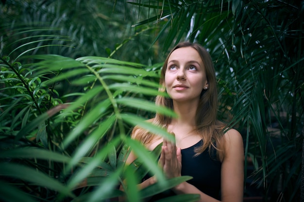 Porträt der niedlichen jungen Frau, die im Dschungel meditiert und namaste Hand tut.