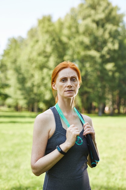 Porträt der reifen Frau der ernsthaften Passform, die das Springseil um den Hals im schönen Park hält, Fitness außerhalb