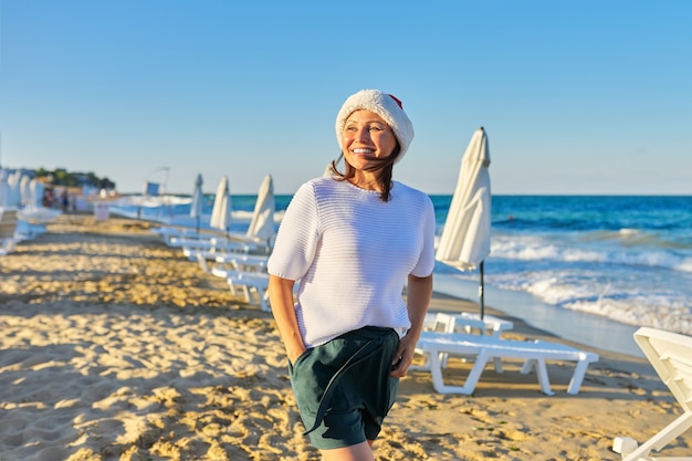 Porträt der reifen glücklichen Frau im Weihnachtsmannhut auf dem Strandseebad