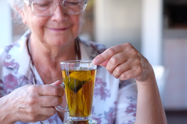 Porträt der schönen älteren Frau im Café, Kräutertee genießend. Entspannte grauhaarige Menschen