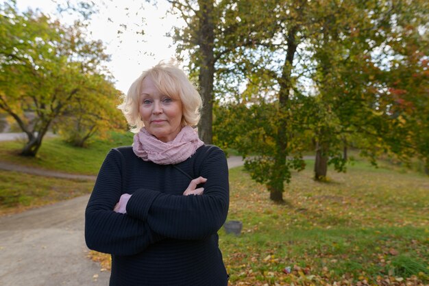 Porträt der schönen älteren Frau mit den kurzen blonden Haaren, die im Park draußen im Herbst entspannen