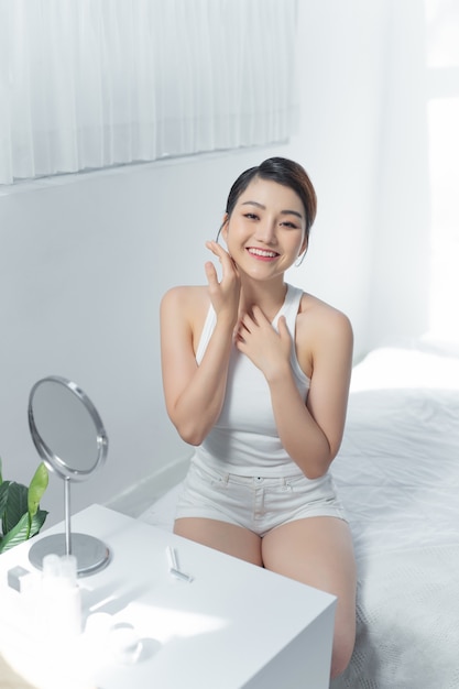 Porträt der schönen asiatischen Frau mit attraktivem Lächeln genießen frische Bettwäsche in der weißen Schlafzimmerwohnung