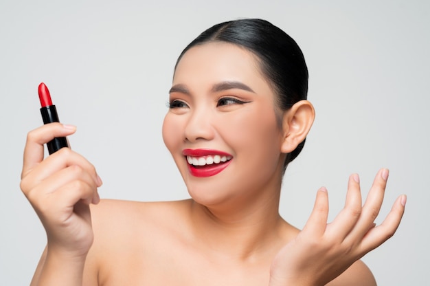 Porträt der schönen asiatischen Frau mit Lippenstift in der Hand