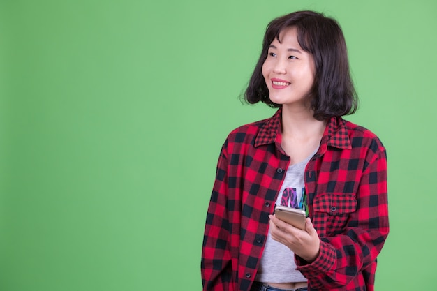 Porträt der schönen asiatischen Hipsterfrau mit kurzen Haaren gegen Chroma Key oder grüne Wand