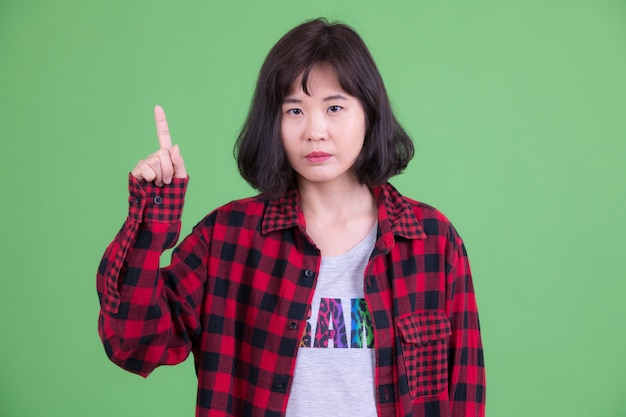 Porträt der schönen asiatischen Hipsterfrau mit kurzen Haaren gegen Chroma Key oder grüne Wand