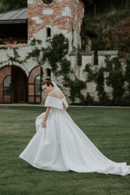 Porträt der schönen Braut im beige Hochzeitskleid mit moderner gelockter Frisur und Schleier, die auf g gehen