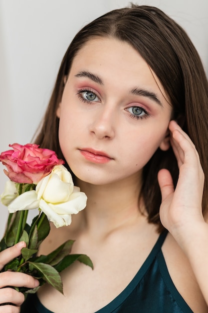 Porträt der schönen dunkelhaarigen Frau mit Blumen. Modefoto, hübsches kleines Mädchen mit rosa Rose