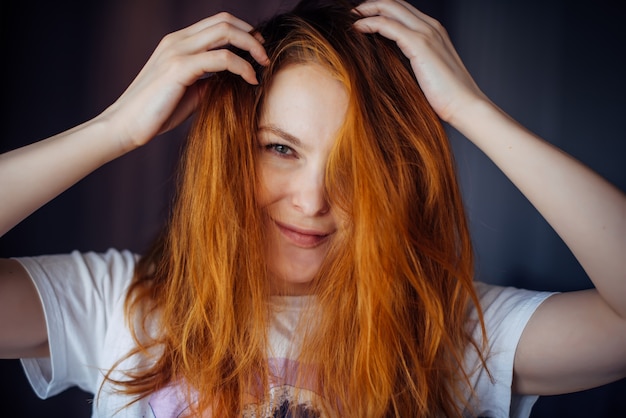 Foto porträt der schönen erwachsenen jungen frau mit dem roten zerzausten haar, nahaufnahme, unscharfer hintergrund. sexy brünette berührt ihr langes haar und schaut in die kamera.