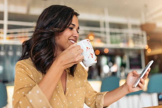 Porträt der schönen Frau, die Mobile in der Kaffeestube verwendet.