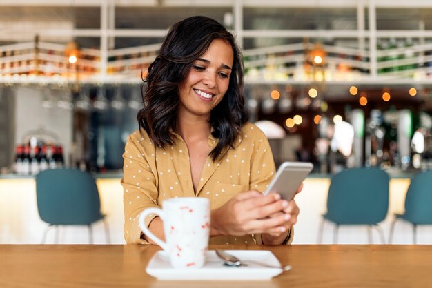 Porträt der schönen Frau, die Mobile in der Kaffeestube verwendet.