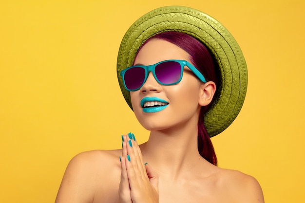 Porträt der schönen Frau mit hellem Make-up, Hut und Sonnenbrille auf gelbem Studiohintergrund. Stilvolle und modische Make und Frisur. Farben des Sommers. Schönheit, Mode und Anzeigenkonzept.