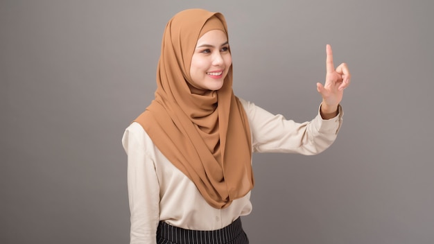 Porträt der schönen Frau mit Hijab berührt virtuellen Bildschirm auf grauer Wand