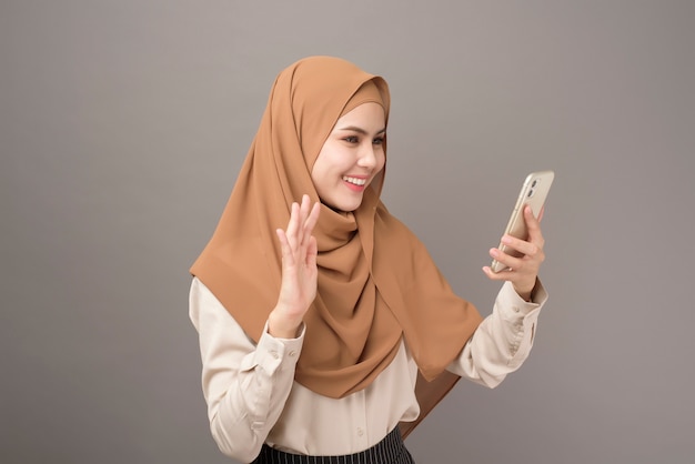 Porträt der schönen Frau mit Hijab unter Verwendung des Handys auf grauem Hintergrund