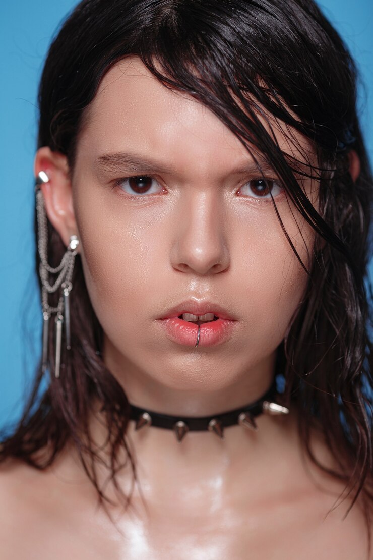 Porträt der schönen gotischen Frau mit Piercings und anderen Accessoires auf Blau