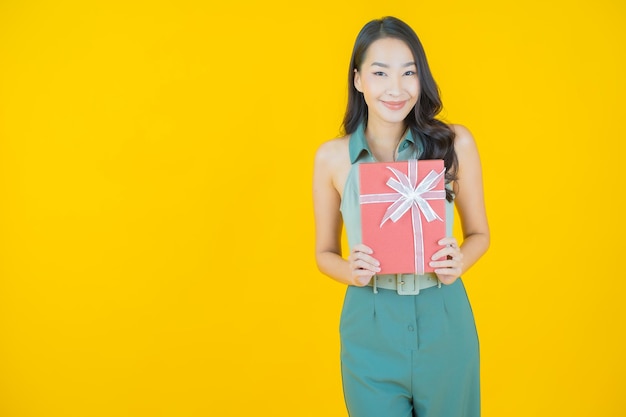 Porträt der schönen jungen asiatischen frau lächelt mit roter geschenkbox auf gelber wand