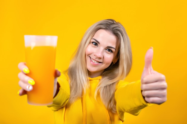 Porträt der schönen jungen blonden Frau, die Orangensaftglas hält, zeigt Daumen hoch, Zeichen OK zur Kamera, lächelndes Mädchen isoliert.