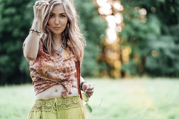 Porträt der schönen jungen Frau, die bohostyle Kleidung trägt, die in den Strahlen der Abendsonne, Sonnenuntergang aufwirft. Mode im Boho-Stil, Frau, die Silberschmuck trägt, der Spaß im Park im Freien hat.