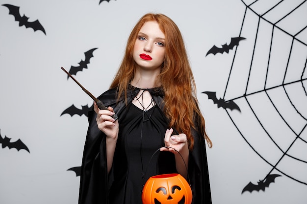 Porträt der schönen kaukasischen Hexe, die orange Kürbis für das Feiern von Halloween hält.