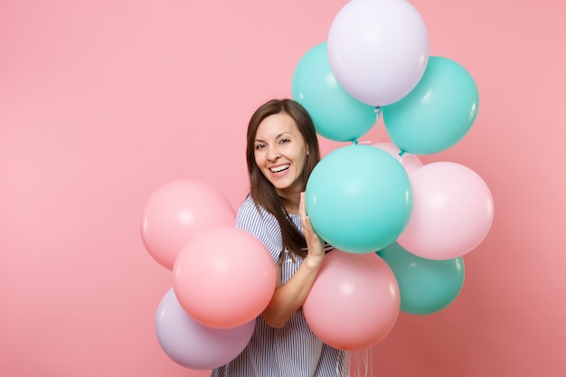 Porträt der schönen lächelnden jungen glücklichen Frau, die blaues Kleid trägt, das bunte Luftballons einzeln auf hellem rosafarbenem Hintergrund hält. Geburtstagsfeier, Konzept der aufrichtigen Emotionen der Menschen.