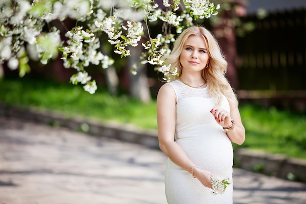 Porträt der schönen schwangeren Frau im blühenden Park. Junge glückliche schwangere Frau, die das Leben in der Natur genießt.