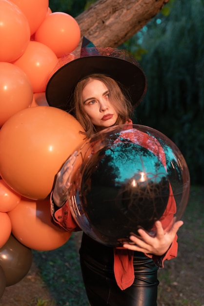 Porträt der schönen sexy jungen Frau im Hexenhalloween-Kostüm mit orange und schwarzen Luftballons