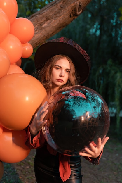 Porträt der schönen sexy jungen Frau im Hexenhalloween-Kostüm mit orange und schwarzen Luftballons