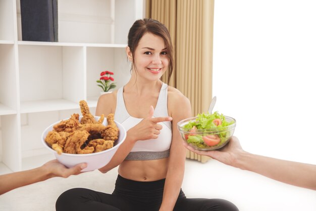 Porträt der schönen sportlichen Frau, die eine Schüssel Salat als gebratenes Huhn für gesundes Leben wählt