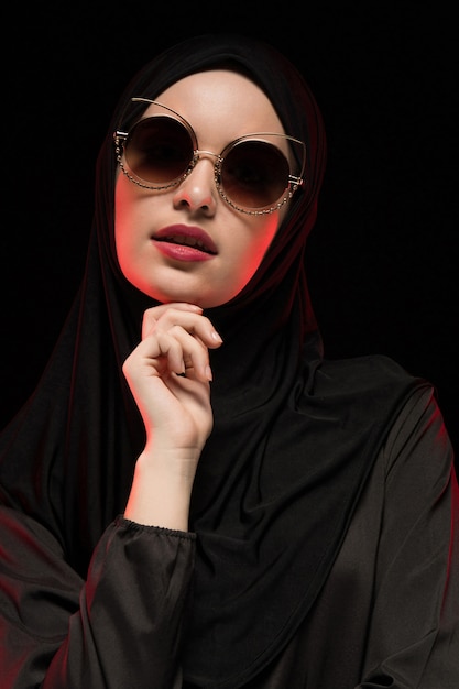 Porträt der schönen stilvollen jungen moslemischen Frau, die schwarzes hijab und Sonnenbrille trägt