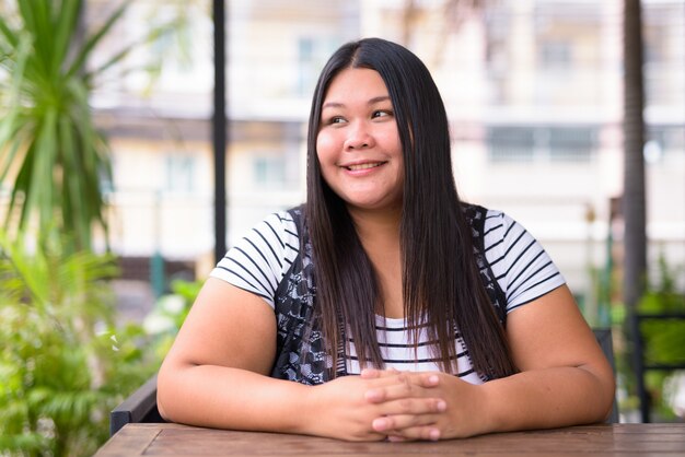 Porträt der schönen übergewichtigen asiatischen Frau, die am Kaffeehaus entspannt