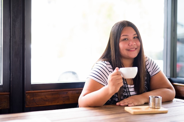 Porträt der schönen übergewichtigen asiatischen Frau, die am Kaffeehaus entspannt