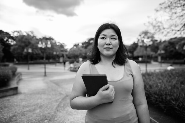 Porträt der schönen übergewichtigen asiatischen Frau, die am Park in der Stadt in Schwarzweiss entspannt