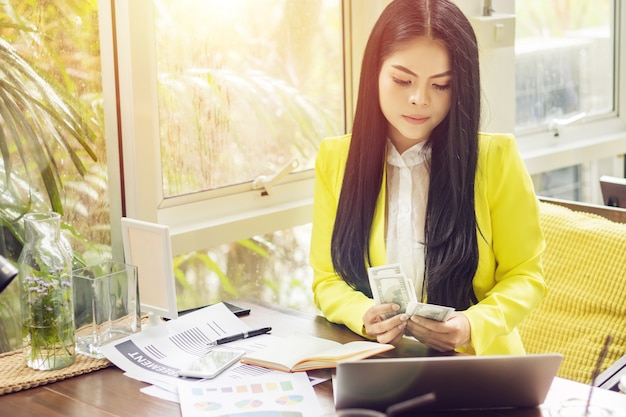 Foto porträt der schönen und überzeugten asiatischen geschäftsfrau beim arbeiten mit notizbuchlaptop und -buch verwalten jobarbeit am arbeitsplatz.