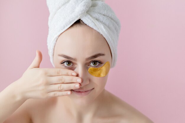 Porträt der Schönheitsfrau mit Augenklappen auf rosa Wand. Frauenschönheitsgesicht mit Maske unter den Augen. Schöne Frau mit natürlichem Make-up und Goldkosmetik-Kollagenpflastern auf frischer Gesichtshaut.