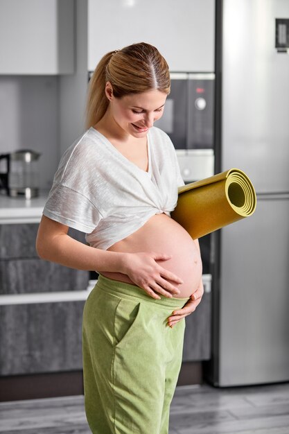 Porträt der schwangeren Frau im weißen T-Shirt und in der grünen Hose, die den Bauch umarmt