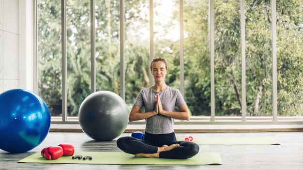 Porträt der Sportfrau in der Sportbekleidung sitzen entspannen und Yoga-Fitnessübung mit blauem Fitball zu Hause üben