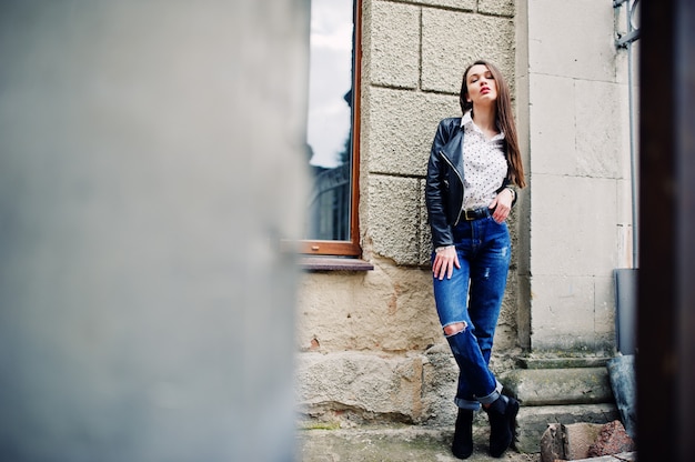 Porträt der stilvollen jungen Frau, die auf Lederjacke und zerrissenen Jeans an den Straßen der Stadt trägt