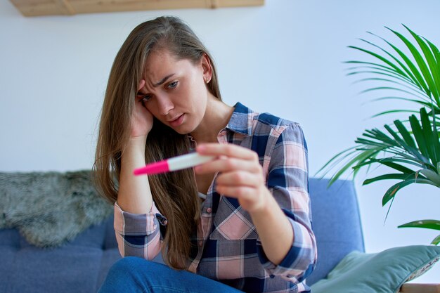 Porträt der traurigen nachdenklichen Frau, die Kopf hält und Schwangerschaftstestergebnis betrachtet