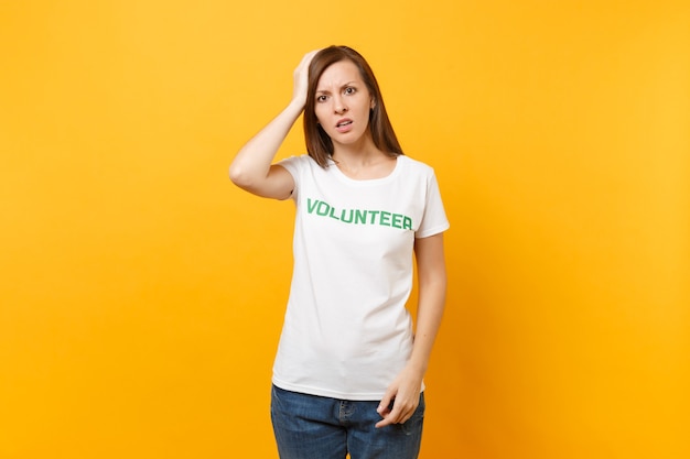 Porträt der traurigen verärgerten schockierten jungen Frau im weißen T-Shirt mit der schriftlichen Aufschrift grüner Titelfreiwilliger lokalisiert auf gelbem Hintergrund. Freiwillige kostenlose Hilfe, Konzept der Wohltätigkeitsarbeit.