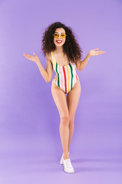Porträt der trendigen attraktiven Frau mit dem lockigen Haar im Badeanzug und in der lachenden Sonnenbrille
